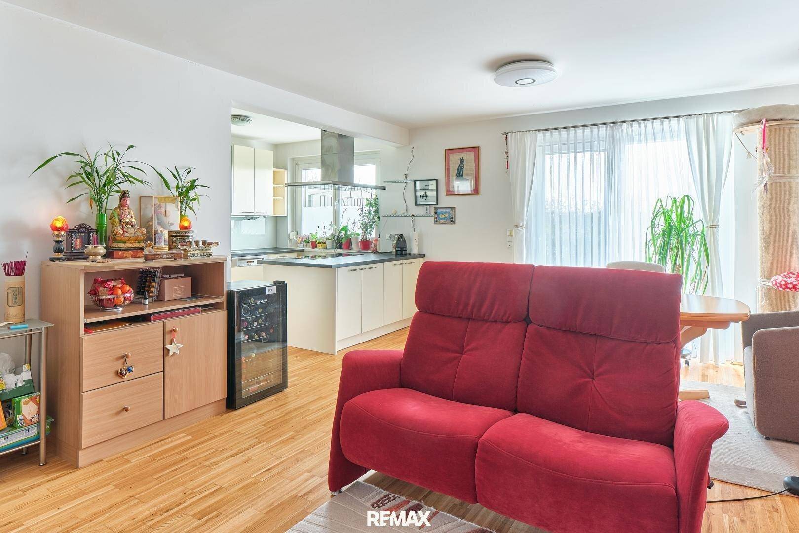 Offener Wohn- und Essbereich mit rotem Sofa, Holzboden und Blick in die Küche.
