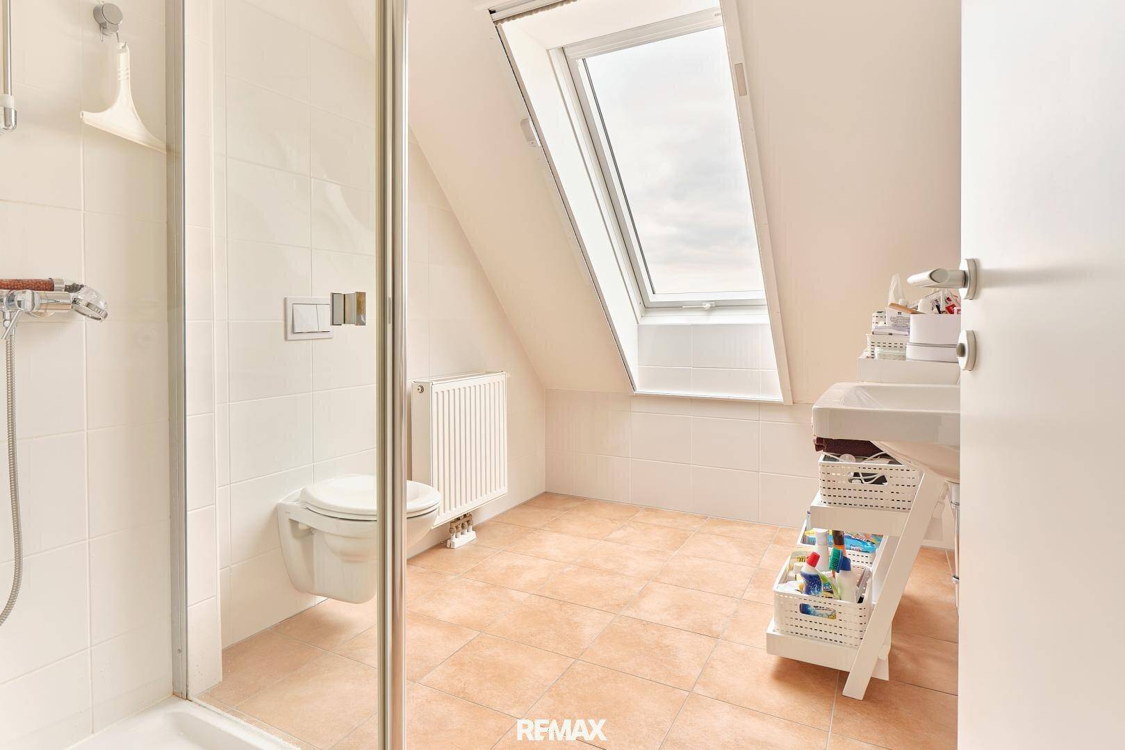 Helles Badezimmer mit Dusche, WC, Waschbecken und einem Dachfenster.