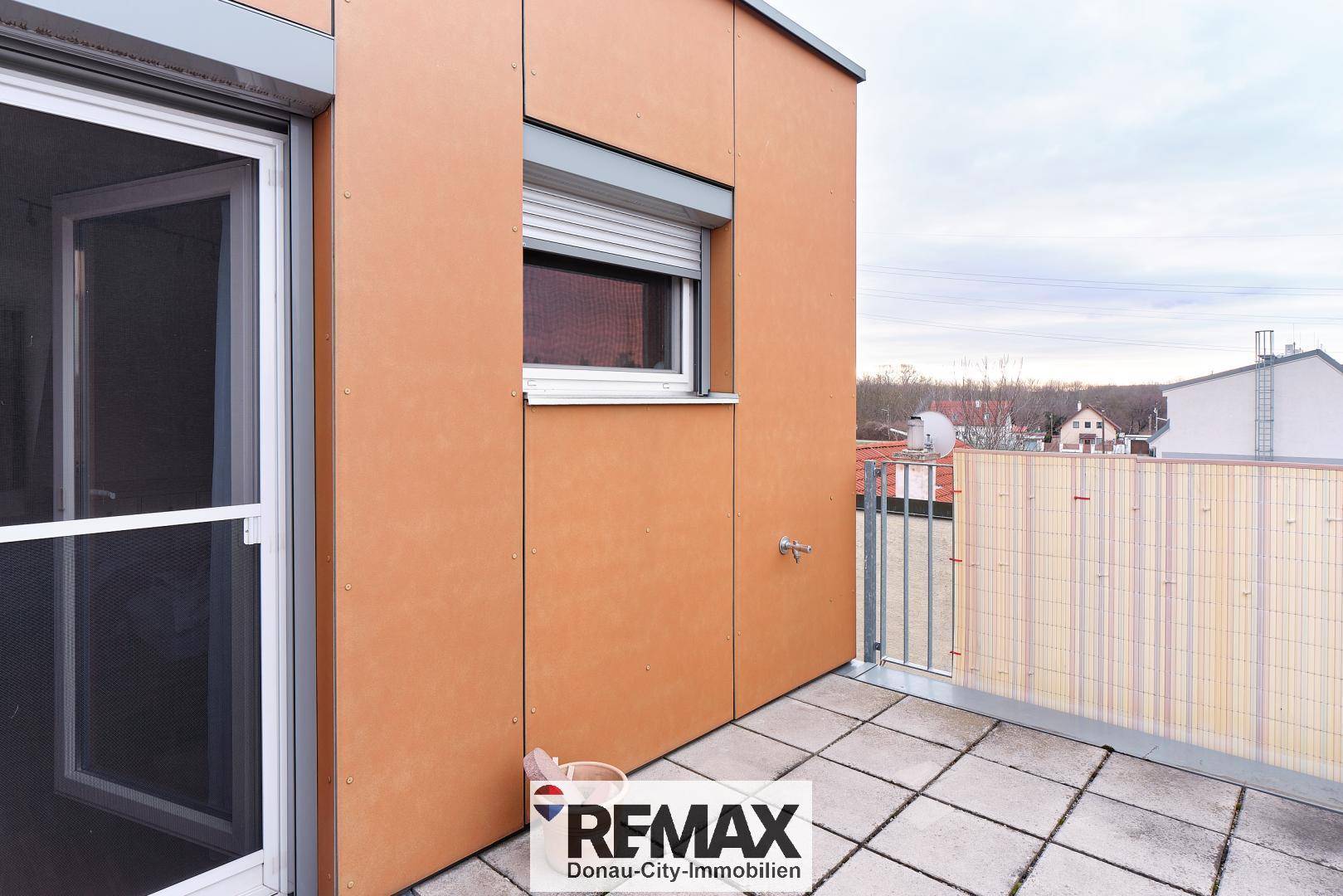 Terrasse mit Fliesenboden, Fenster mit Rollladen und Blick auf die Umgebung.