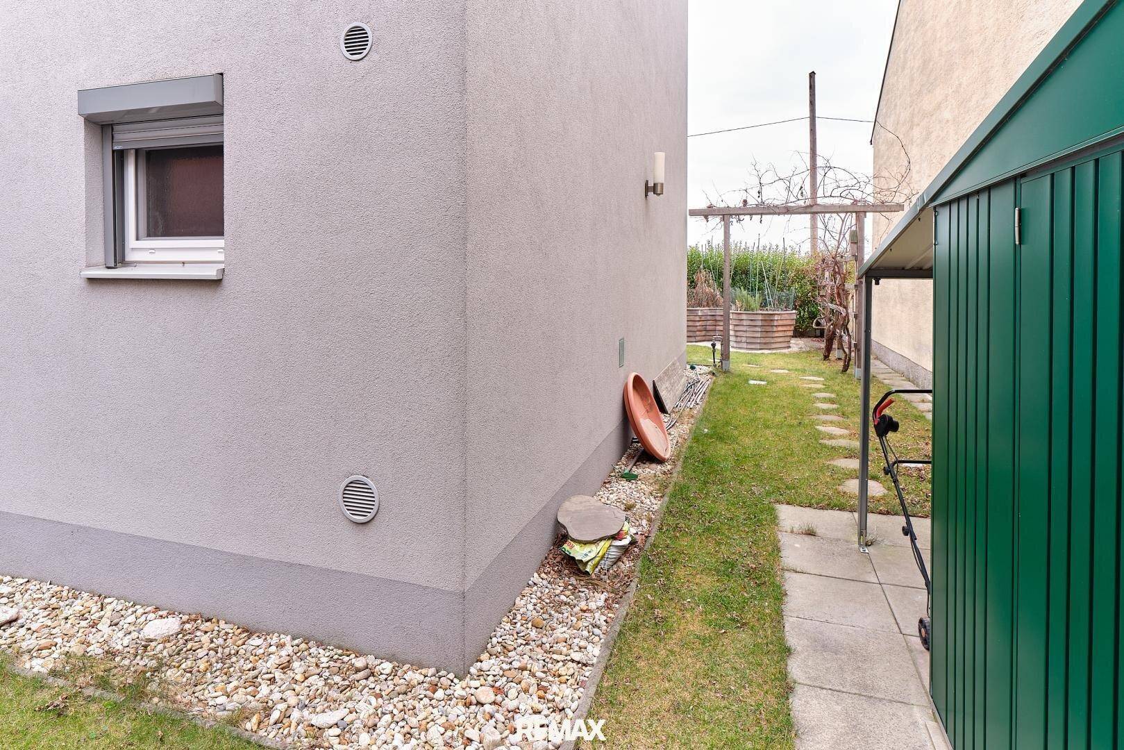 Seitenansicht eines Reihenhauses mit Gartenweg und einem Geräteschuppen.