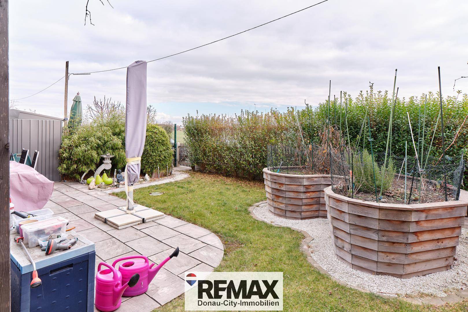 Garten mit Terrasse, Rasenfläche und Hochbeeten für den Anbau von Pflanzen.