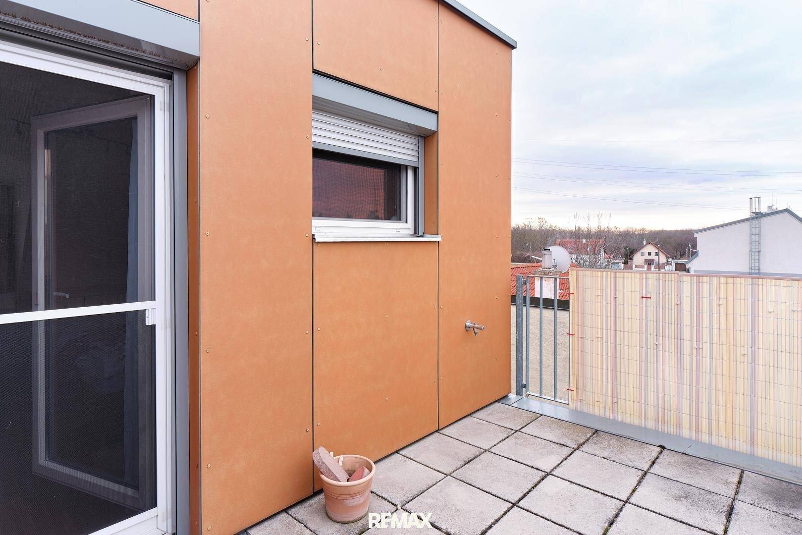 Terrasse mit Zugang zum Innenbereich und einem Fenster mit Rollladen.
