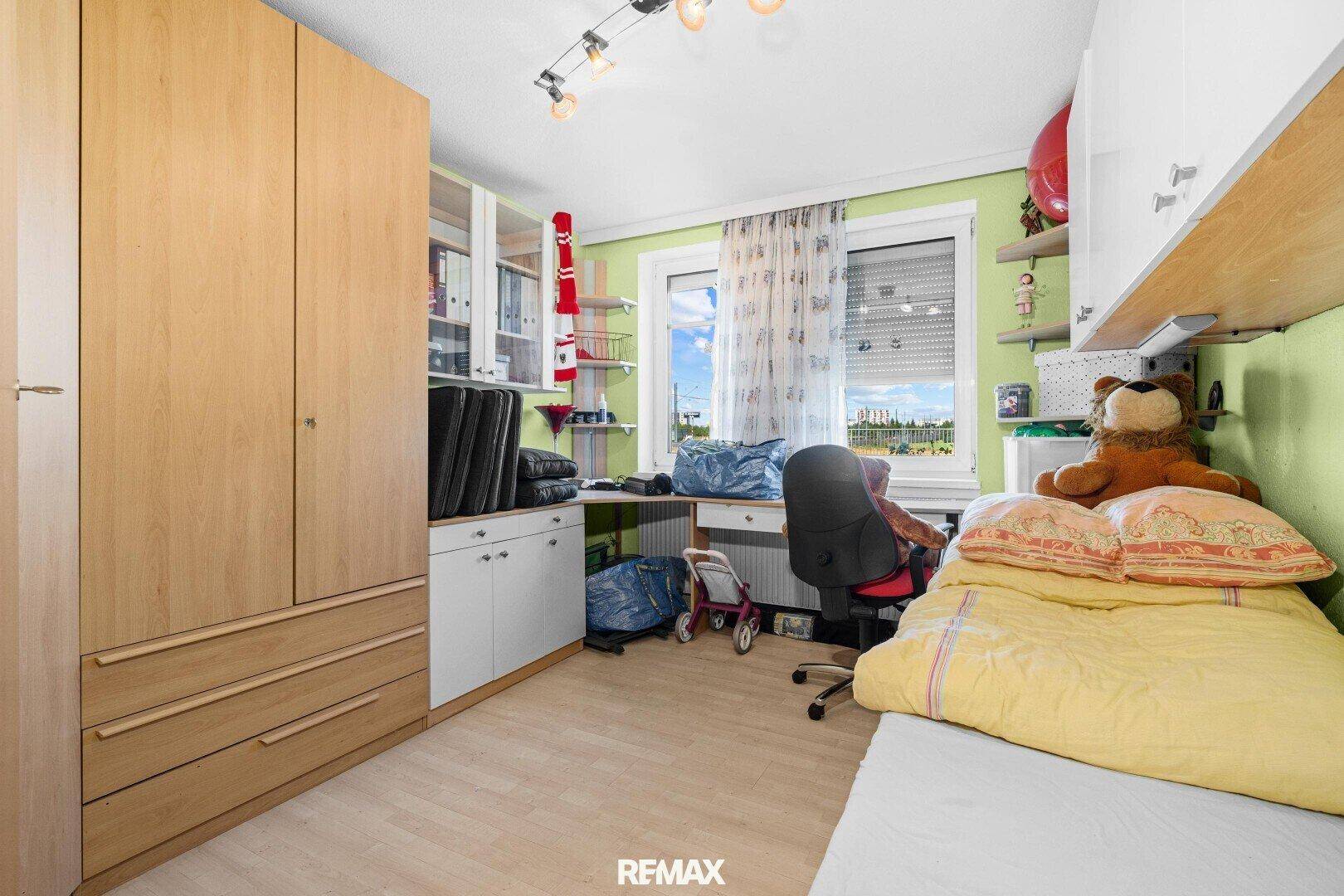 Kinderzimmer mit Einzelbett, Schreibtisch, hellgrünen Wänden und Blick ins Freie.