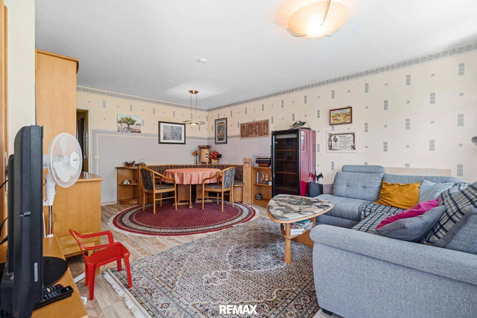 Geräumiger Wohn-Essbereich mit bequemer Couch, rundem Esstisch und traditioneller Tapetendekoration.