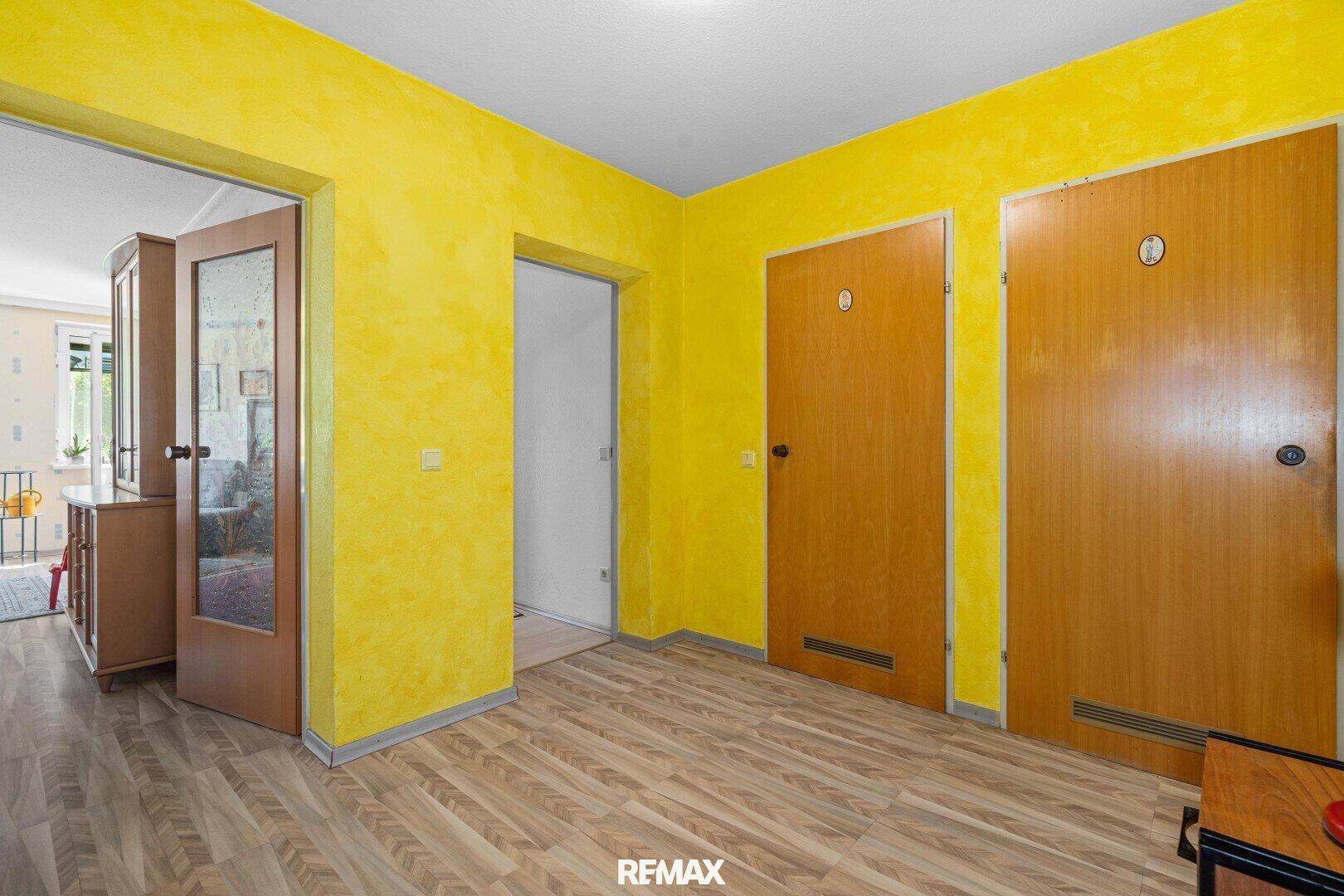 Heller Flur mit auffälligen gelben Wänden und mehreren Holztüren zu den Zimmern.