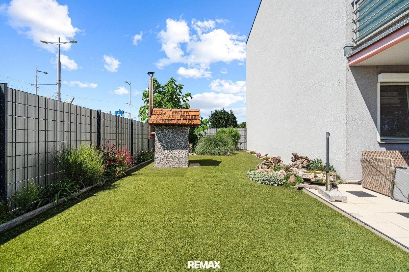Gepflegter Gartenbereich mit Steinofen, Kunstrasen und angrenzender Terrasse.