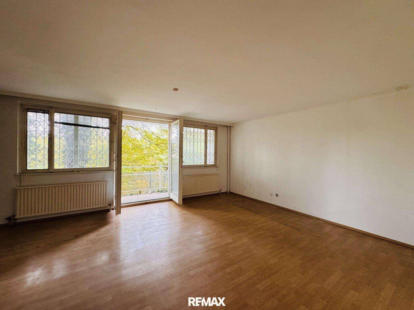 Geräumiges Wohnzimmer mit Holzboden und großen Fenstern, die viel Licht hereinlassen.