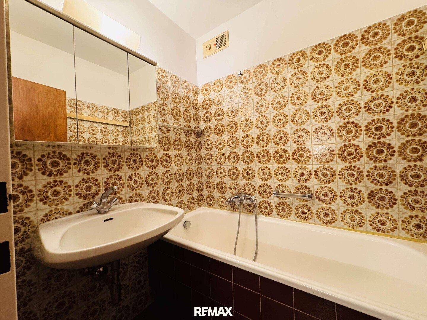 Badezimmer mit Badewanne, Waschbecken und gemusterten Fliesen im Vintage-Stil.