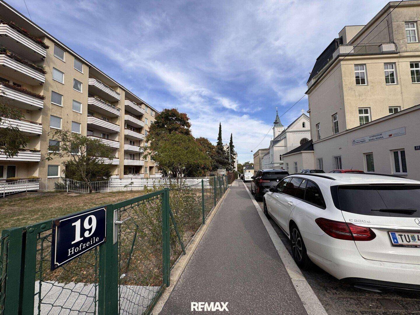 Blick auf die Straße mit parkenden Autos und dem Mehrfamilienhaus auf der linken Seite.