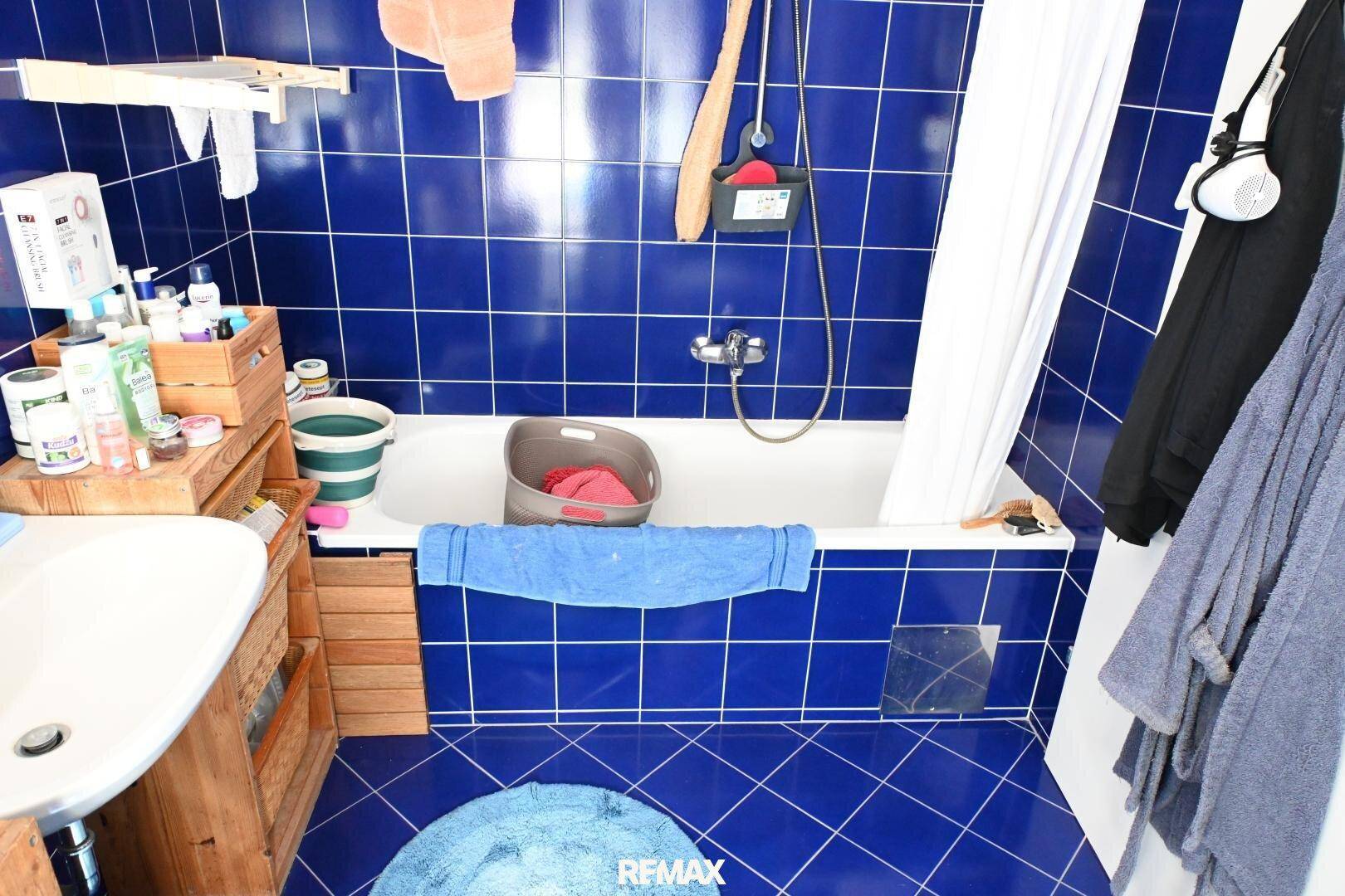 Badezimmer mit blauen Fliesen, Badewanne mit Duschfunktion und Waschbecken, bietet eine praktische Ausstattung.