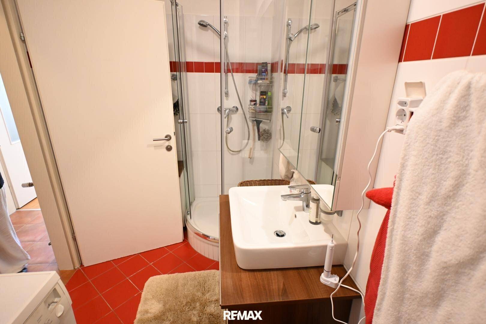 Badezimmer mit weiß-roten Fliesen und moderner Duschkabine, ausgestattet mit einem stilvollen Waschbecken.