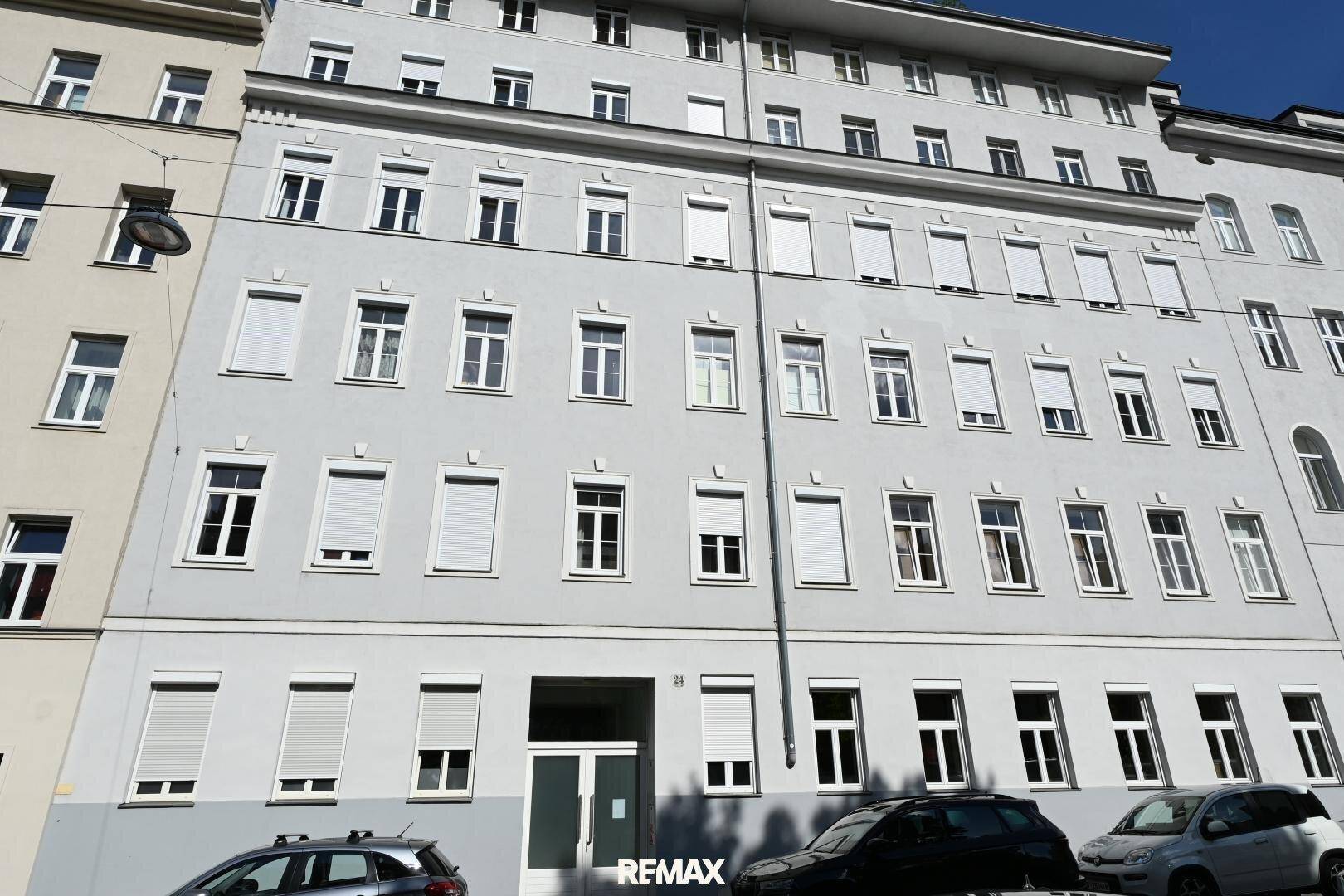 Klassische Fassade eines Mehrfamilienhauses mit zahlreichen Fenstern und Rollläden, in städtischer Umgebung.
