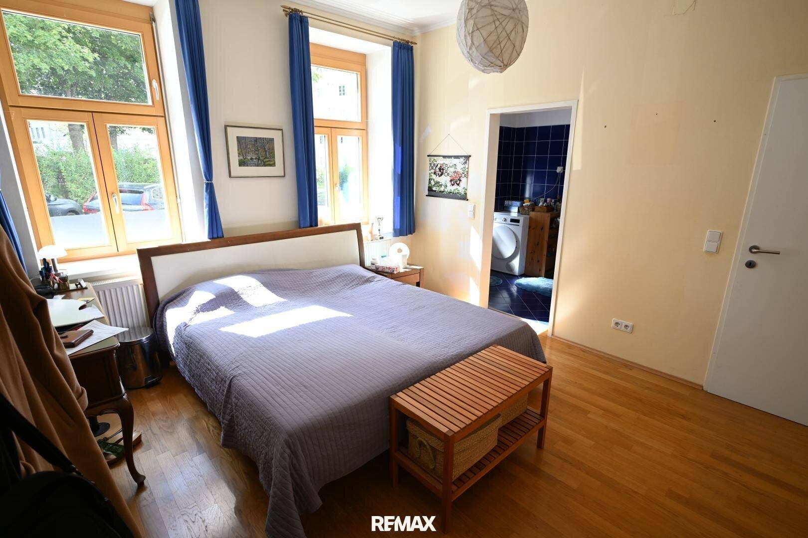 Gemütliches Schlafzimmer mit Doppelbett, Holzboden und blauen Vorhängen, mit direktem Zugang zum Badezimmer.