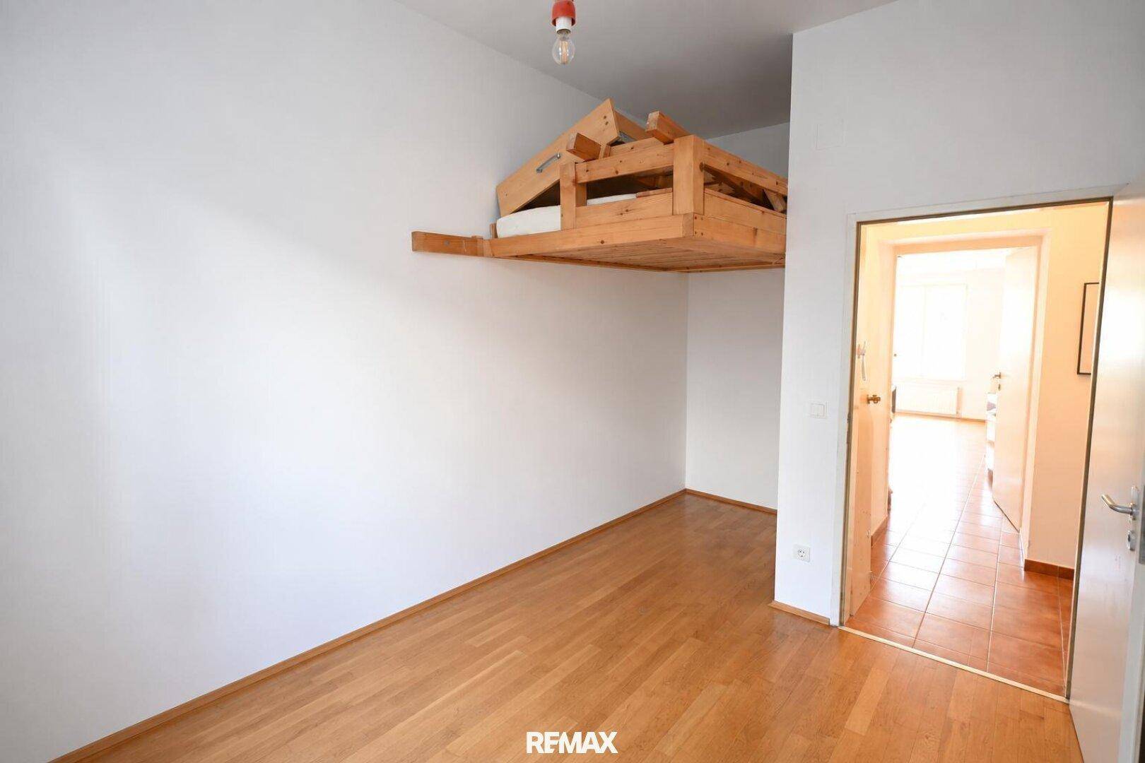 Geräumiges Schlafzimmer mit Holzboden und Hochbett, bietet flexible Nutzungsmöglichkeiten und viel Tageslicht.