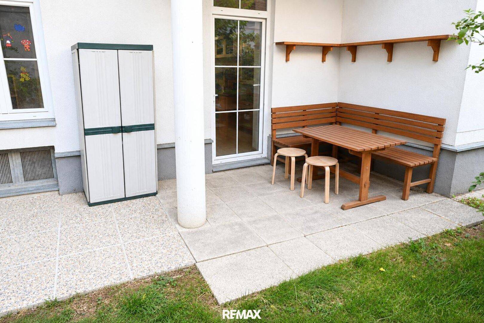 Gepflasterte Terrasse mit Holzsitzgruppe und praktischem Gartenschrank, ideal für Mahlzeiten im Freien.