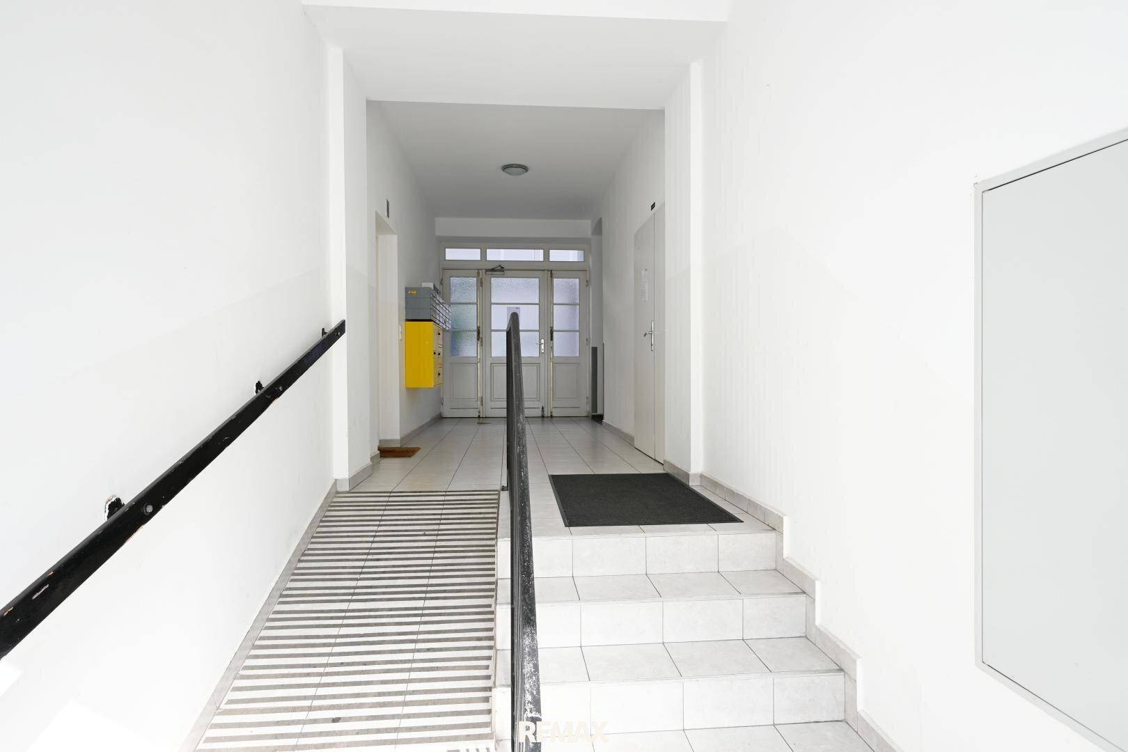 Eingangsbereich eines Gebäudes mit Treppe und barrierefreier Rampe, bietet Zugang zum Haus.