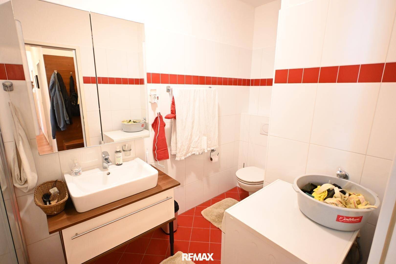 Modernes Badezimmer mit weißen und roten Fliesen, Waschbecken, WC und Waschmaschine, bietet eine frische Optik.