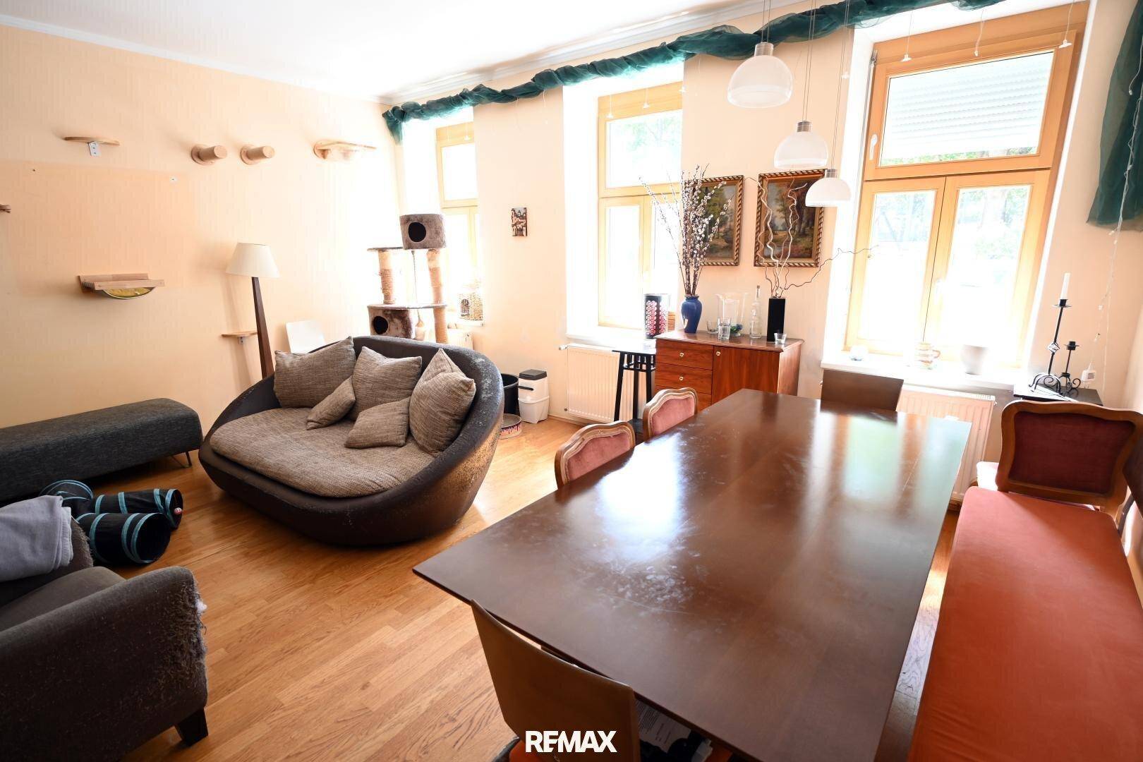 Geräumiger Wohn-Essbereich mit Holzboden, großem Esstisch und bequemer Couch, hell durch große Fenster.