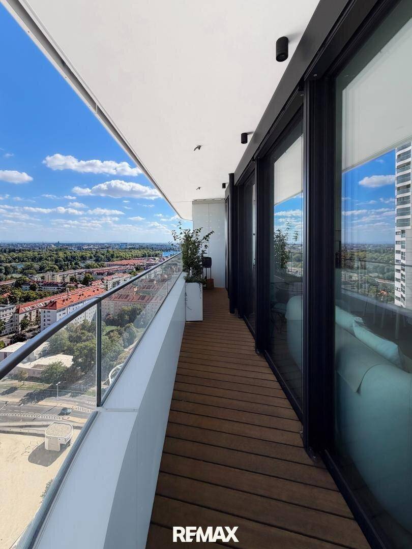 Langer Balkon mit Holzdeck, Glasgeländer und weitem Blick über die Stadt.