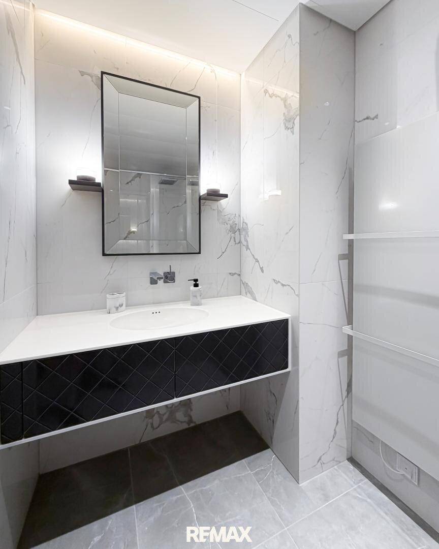 Modernes Badezimmer mit Marmorfliesen, elegantem Waschtisch und großem Spiegel.