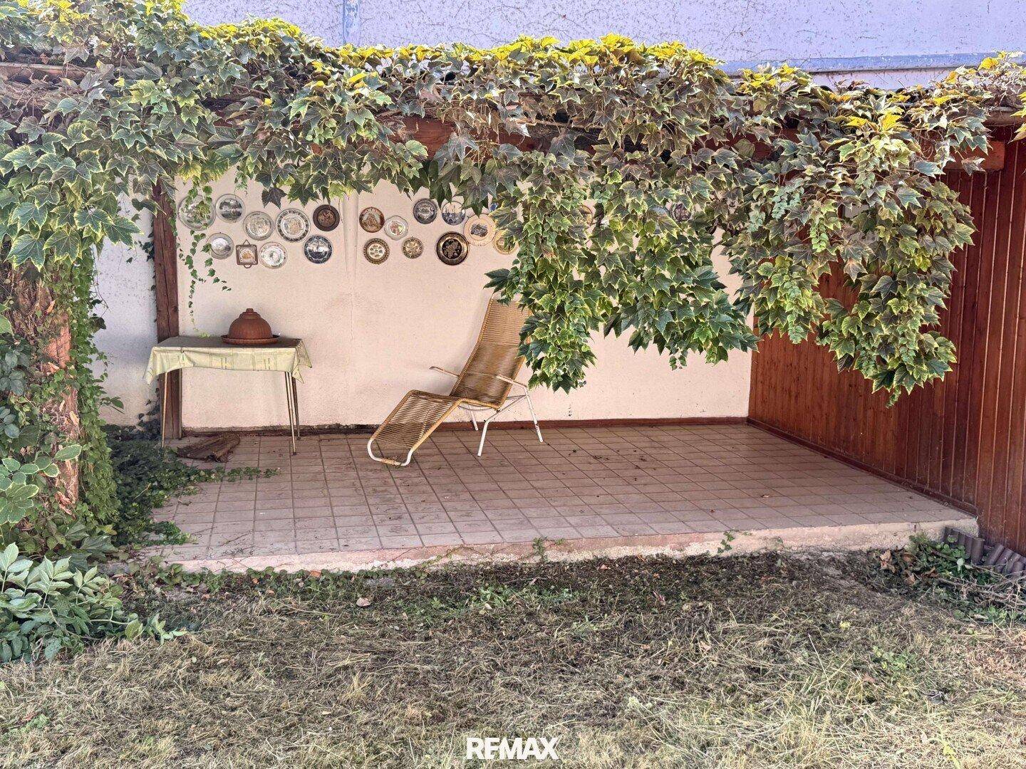 Überdachte Terrasse mit Fliesenboden, Liegestuhl und dekorativen Tellern an der Wand.