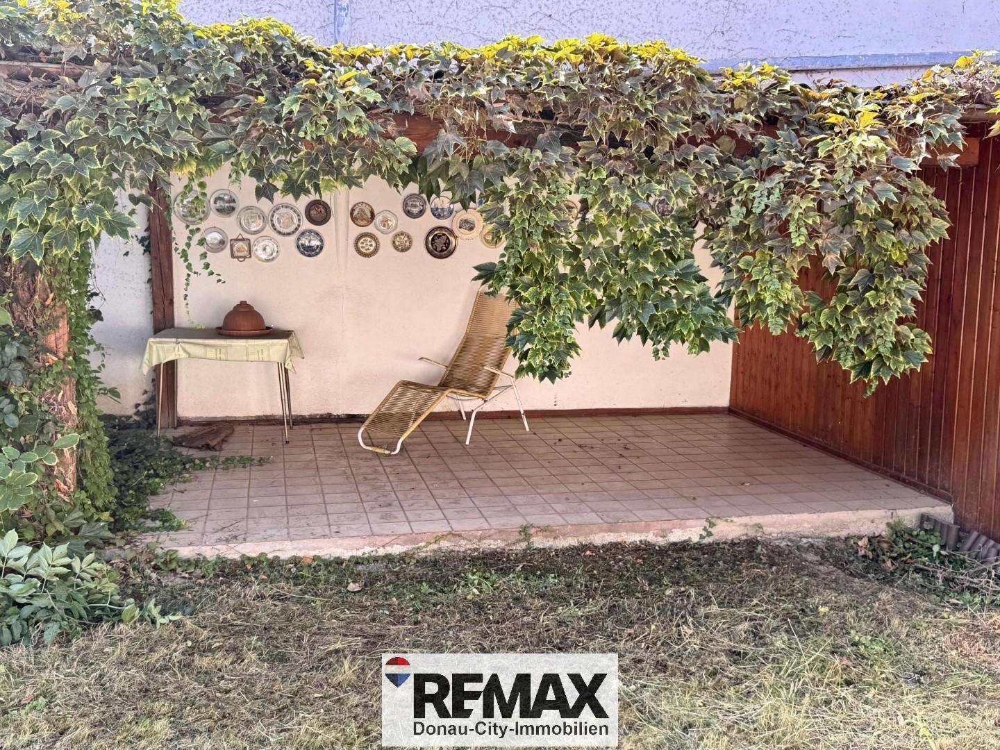 Gemütlicher Gartenbereich mit überdachter Terrasse, Liegestuhl und Dekoration.