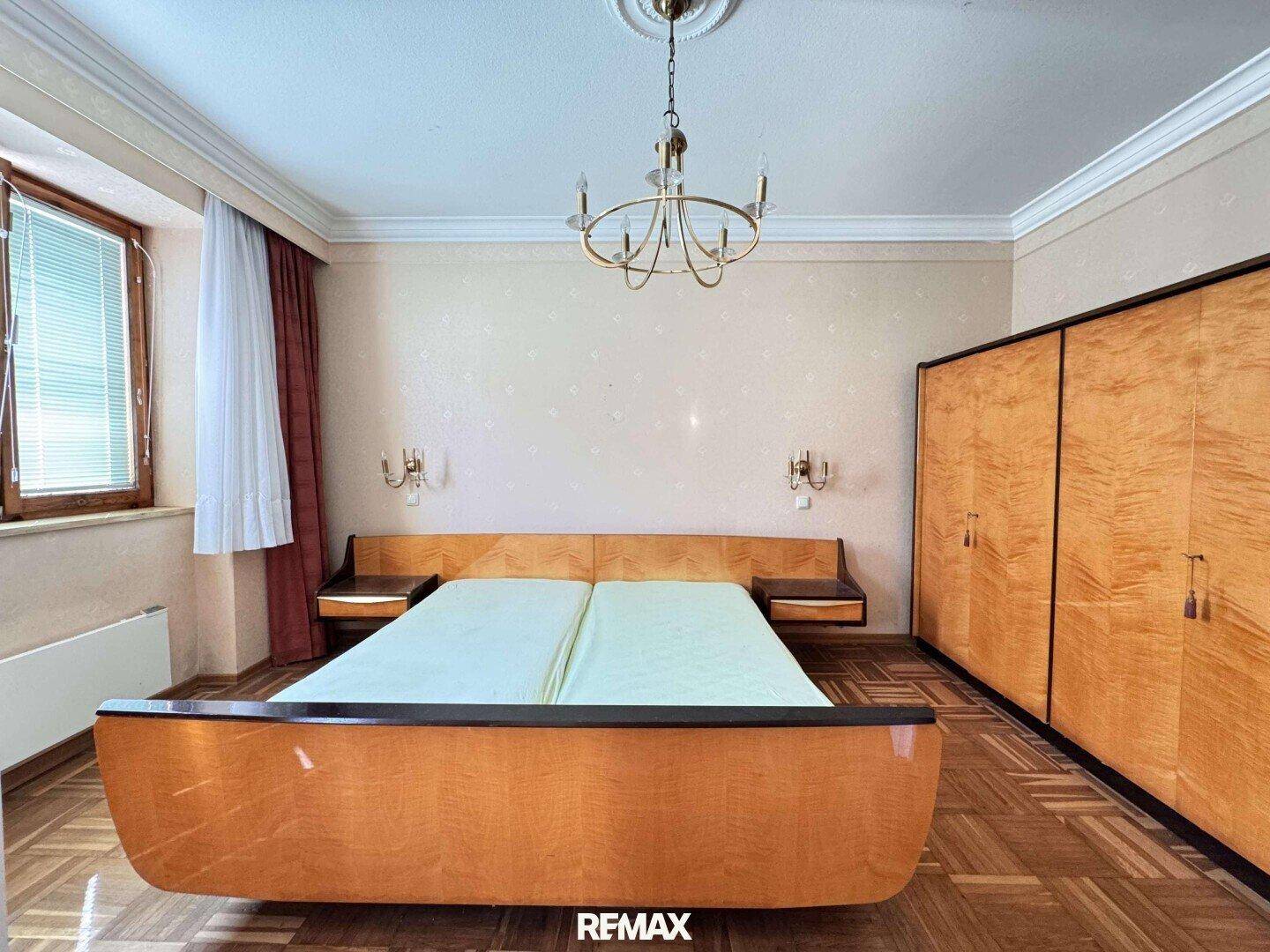 Schlafzimmer mit Doppelbett, Holzschrank und Kronleuchter, im Stil der 50er Jahre.