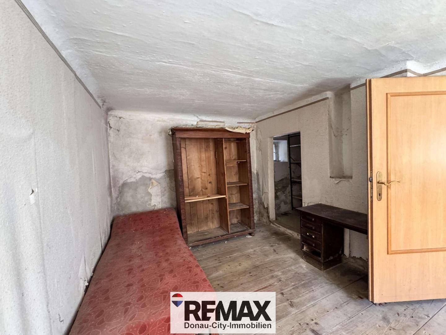 Unrenovierter Raum mit Holzboden, altem Schrank und einfacher Liege.