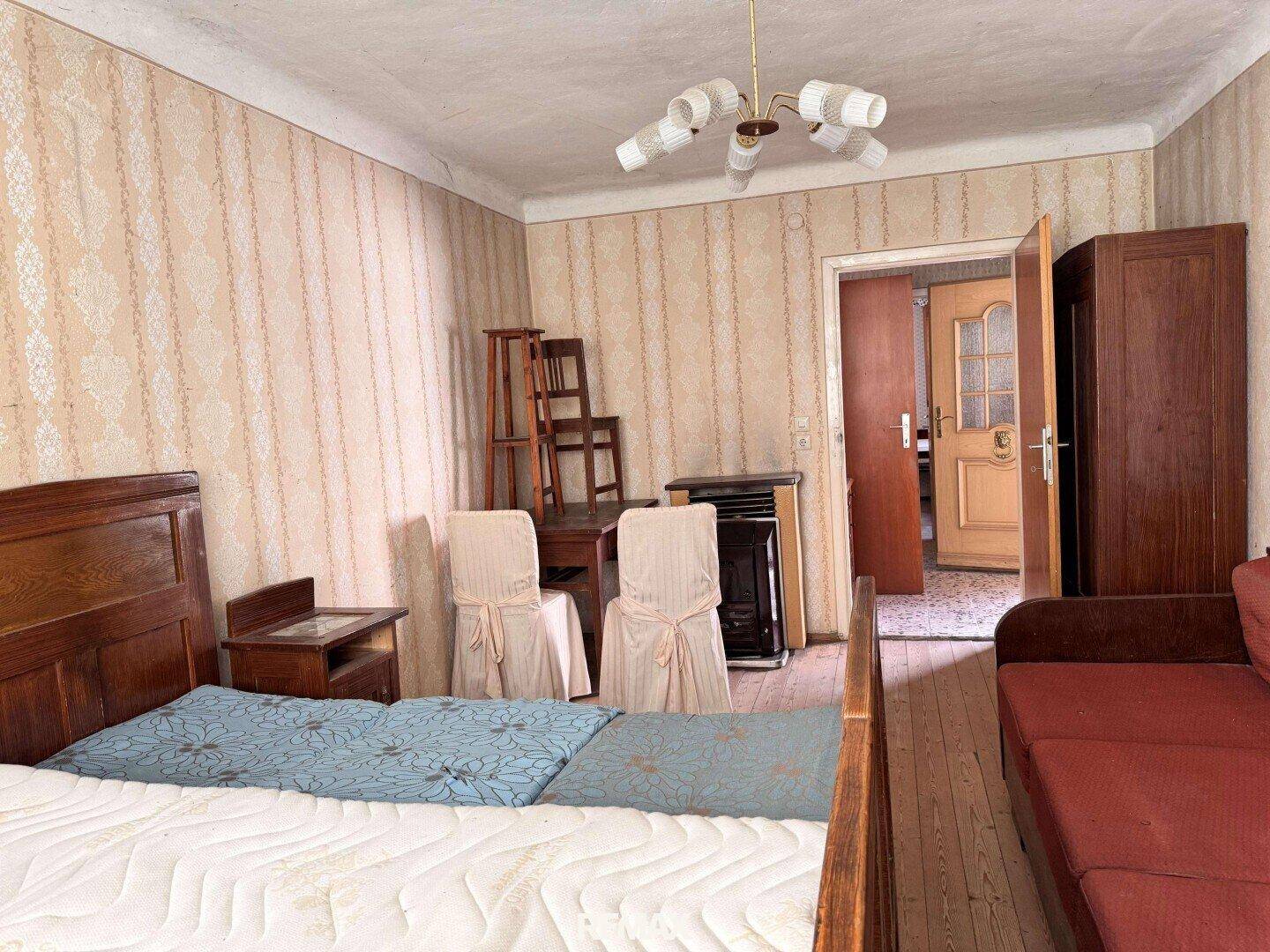 Schlafzimmer mit Einzelbett, gemusterter Tapete und Blick auf einen weiteren Raum.