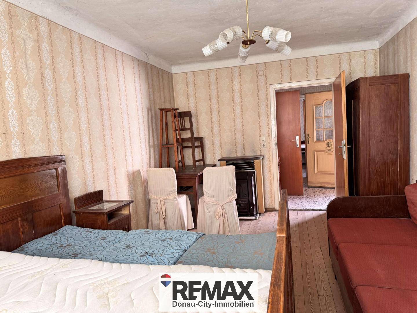 Schlafzimmer mit gemusterter Tapete, Einzelbett und einfacher Einrichtung.