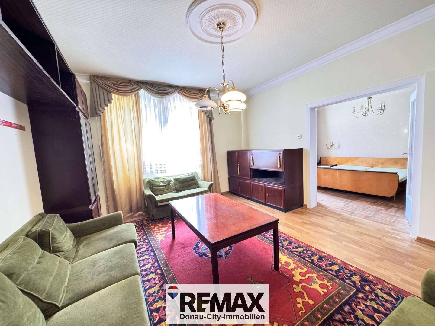 Gemütliches Wohnzimmer mit traditionellen Möbeln, Teppichboden und Blick ins Schlafzimmer.