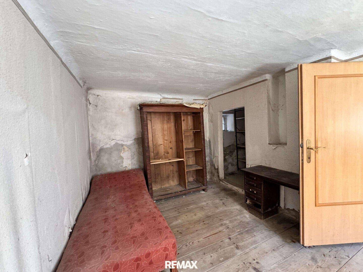 Unrenovierter Raum mit abblätternder Farbe, Holzboden und altem Schrank.