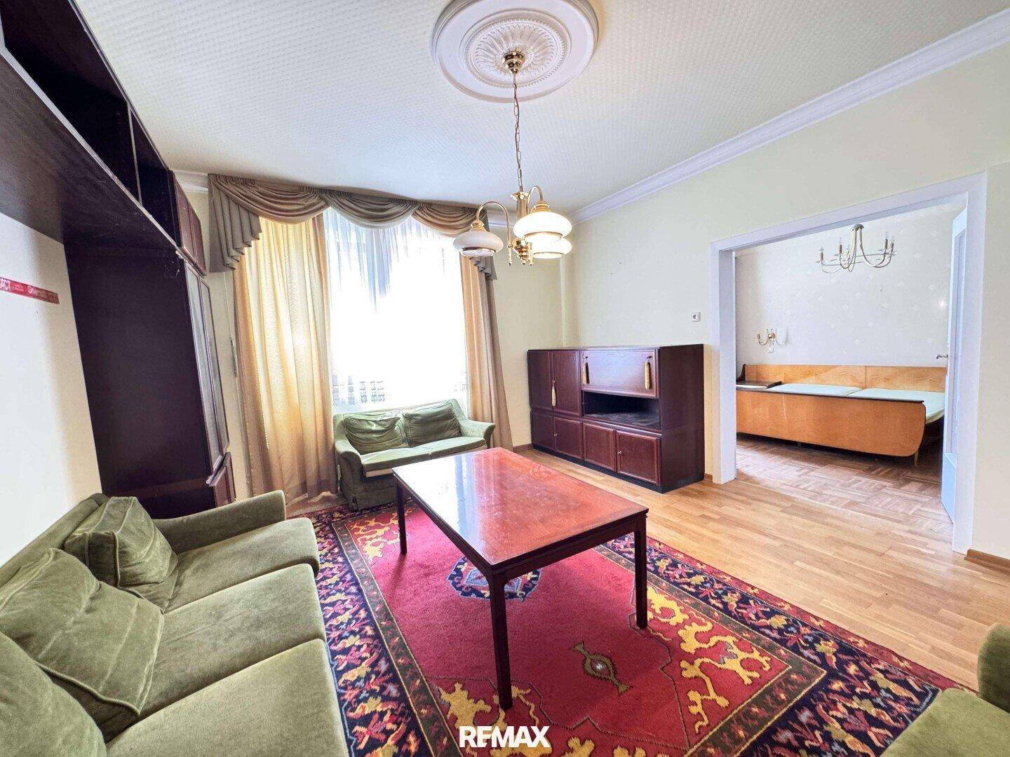 Gemütliches Wohnzimmer mit traditionellem Teppich, grünen Sofas und Blick ins Schlafzimmer.