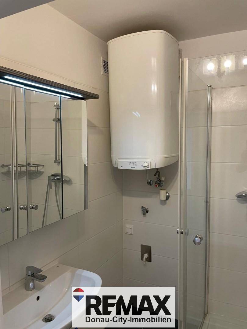 Helles Badezimmer mit Waschbecken, Spiegelschrank und großem Warmwasserboiler an der Wand.