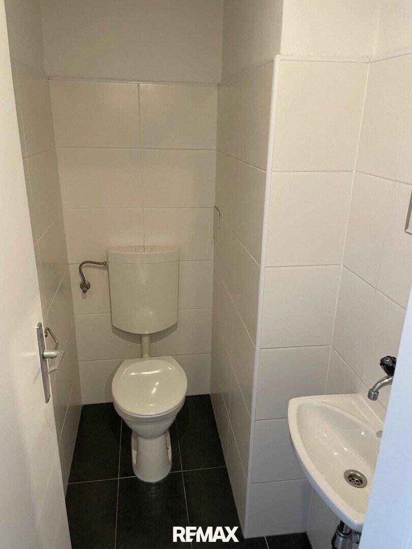 Separates WC mit Toilette, kleinem Handwaschbecken und weißen Wandfliesen.