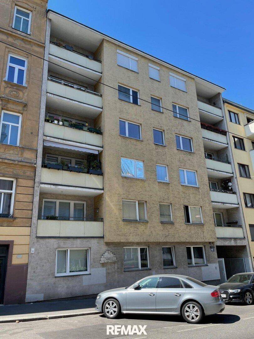 Mehrstöckiges Wohngebäude mit Balkonen und geparkten Autos auf der Straße davor.