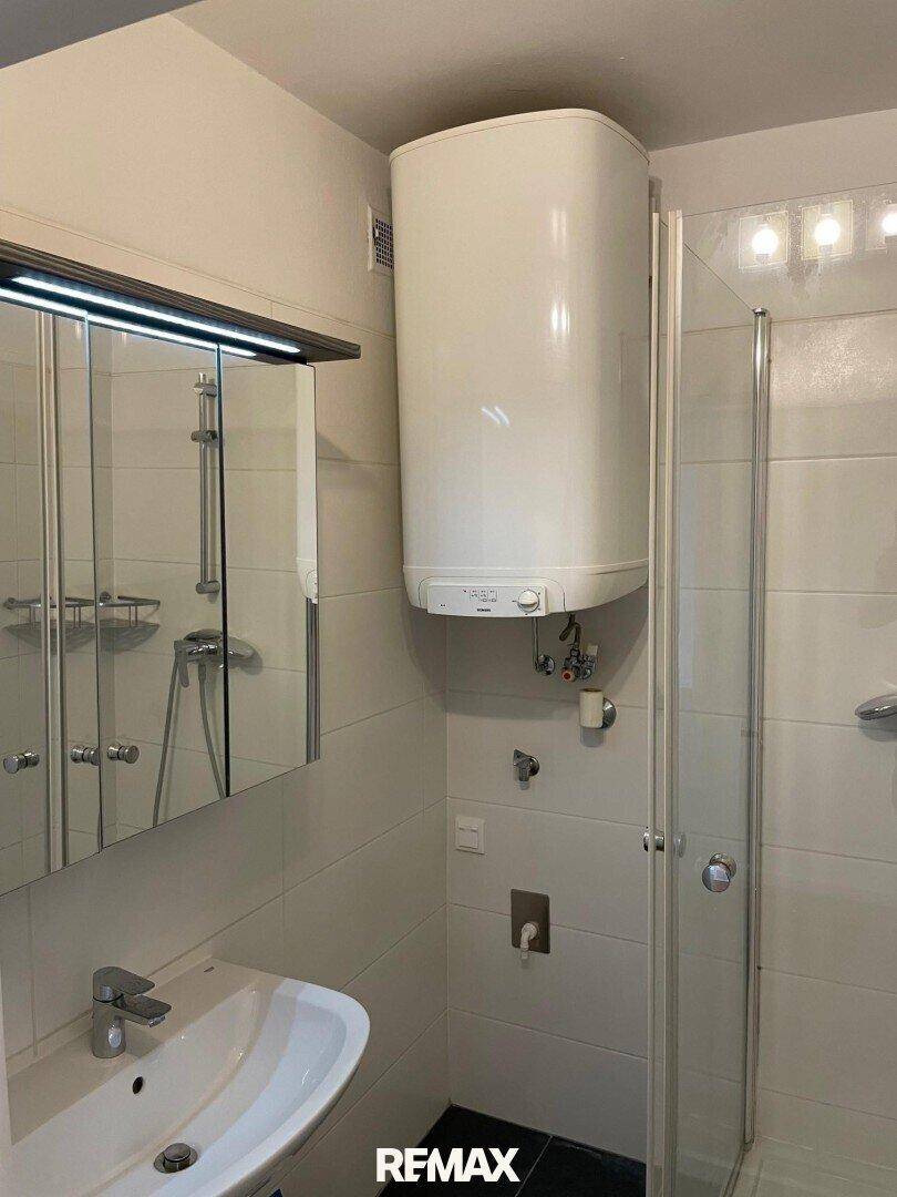 Modernes Badezimmer mit Duschkabine, Waschbecken, Spiegelschrank und Wandboiler.