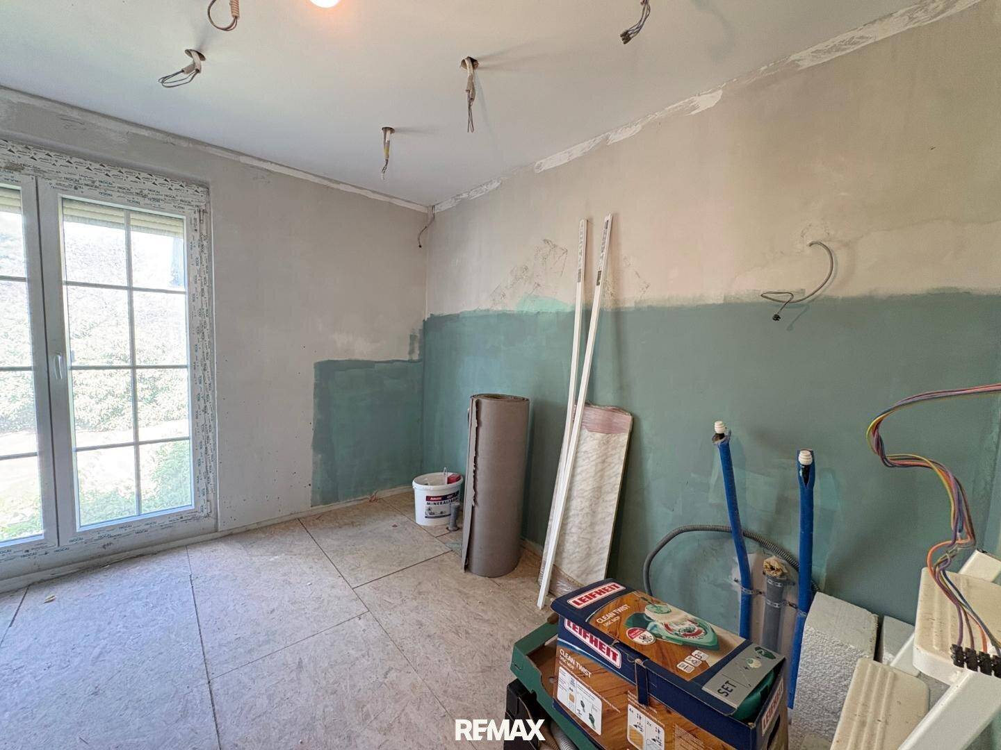 Raum im Rohbau mit grünen Wänden und OSB-Plattenboden, bereit für den Ausbau.
