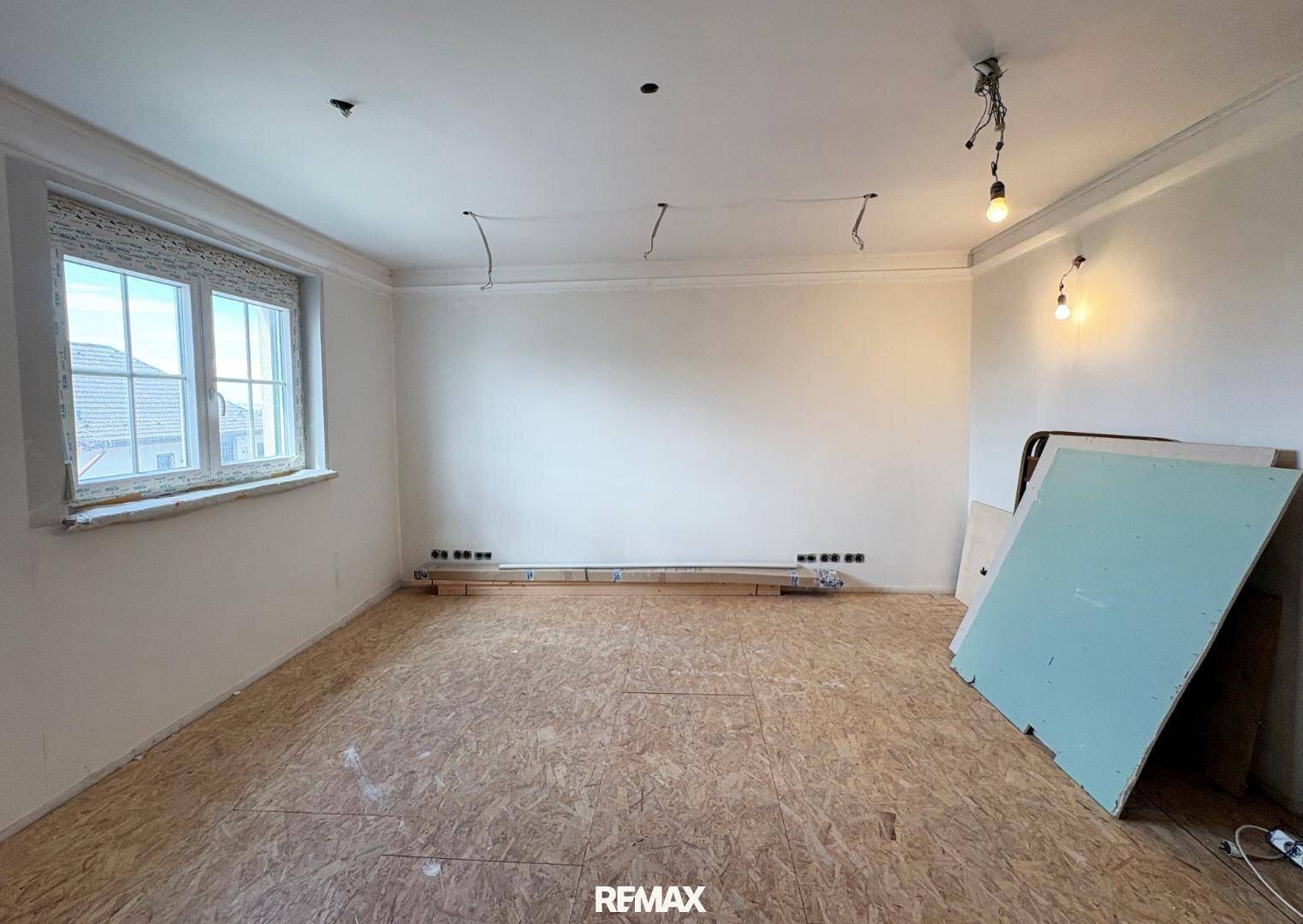 Renovierungsbedürftiger Raum mit OSB-Plattenboden und Fenster, bereit für den Innenausbau.