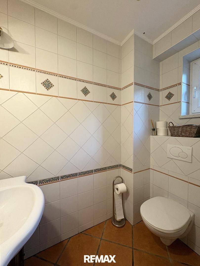 Kleines Gäste-WC mit weißen Fliesen, Wand-WC und Fenster für Tageslicht.
