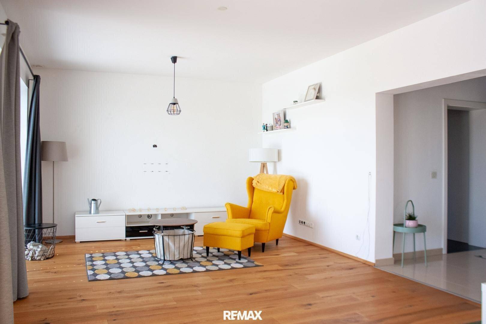 Gemütliches Wohnzimmer mit hellem Holzfußboden, gelbem Sessel und moderner Dekoration.