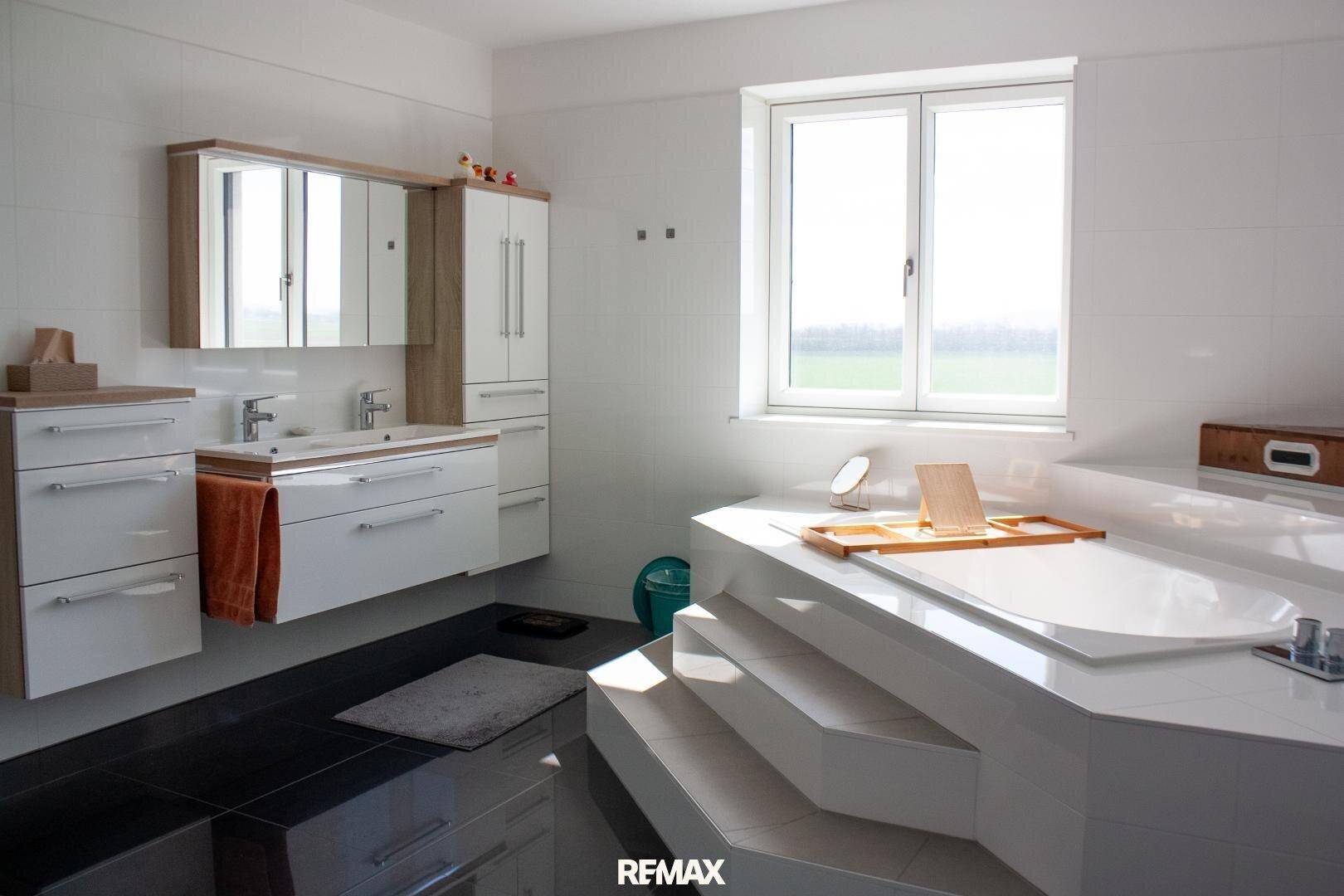 Luxuriöses Badezimmer mit großer Badewanne, Doppelwaschbecken und Fenster für viel Tageslicht.