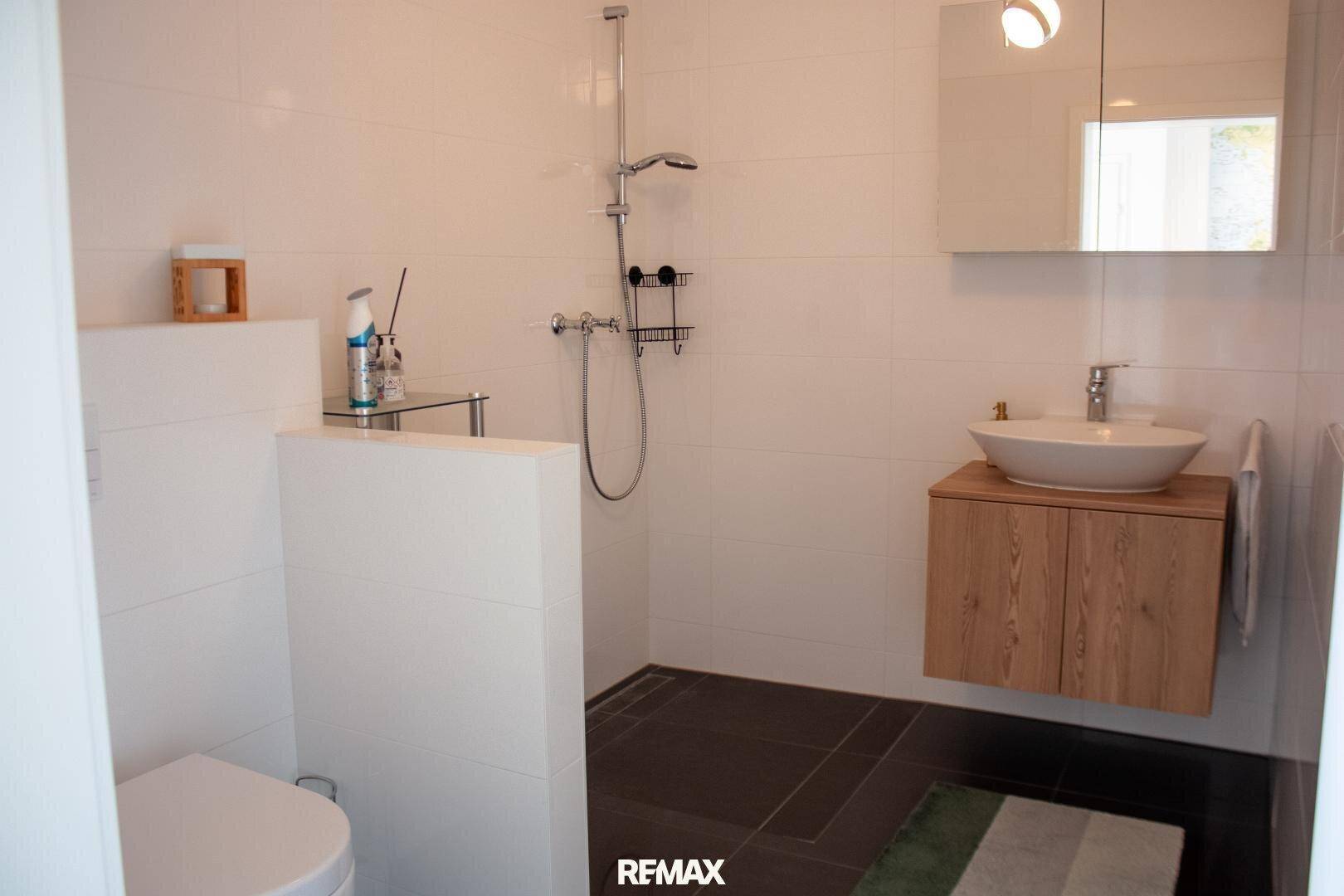Modernes Badezimmer mit ebenerdiger Dusche, wandhängendem WC und Holzwaschtisch.