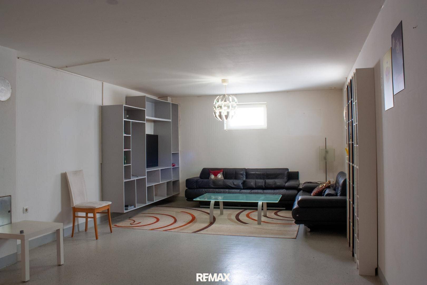 Ausgebauter Keller-Wohnbereich mit Sofa, Regalen und kleinem Fenster für Tageslicht.