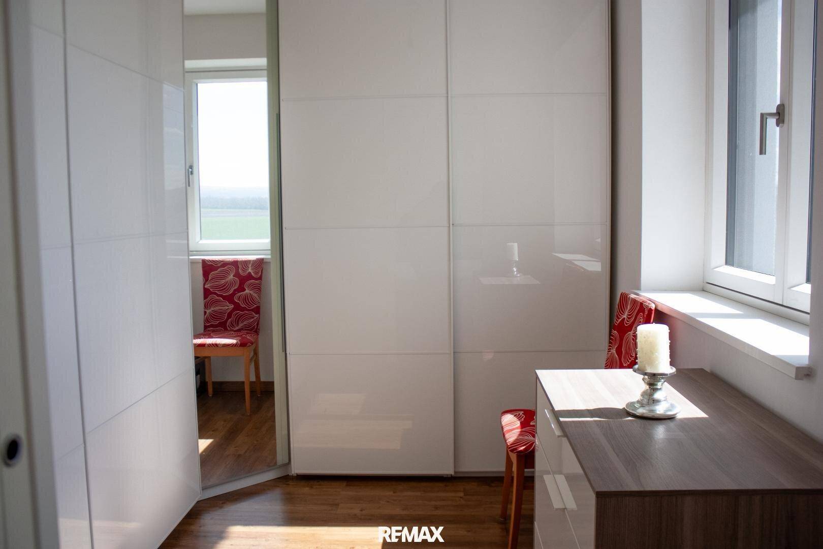 Helles Zimmer mit weißen Schiebetürenschränken und Fenster, ideal als Ankleidebereich.