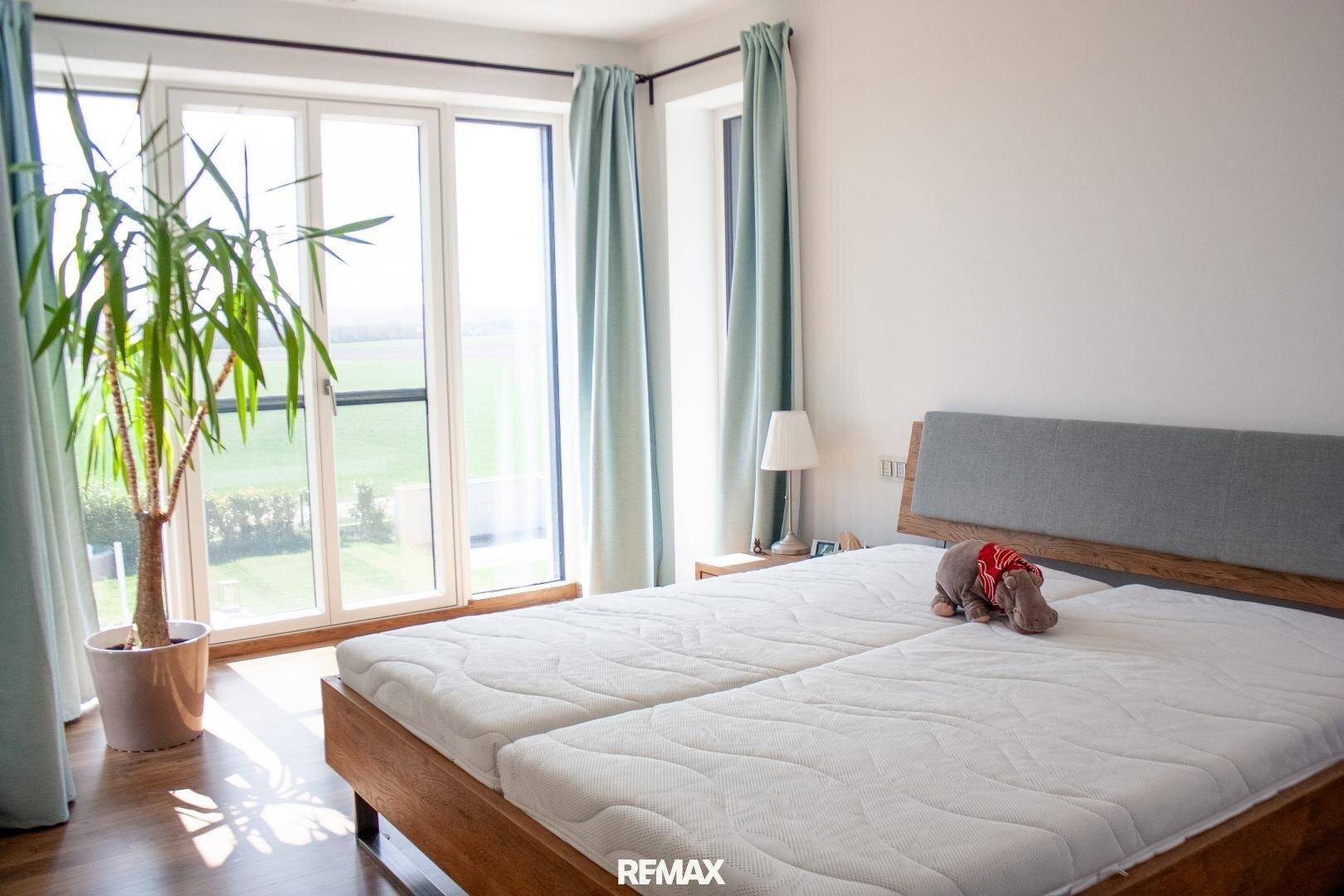 Schlafzimmer mit Doppelbett und großen Fenstern, die einen weiten Blick ins Grüne bieten.
