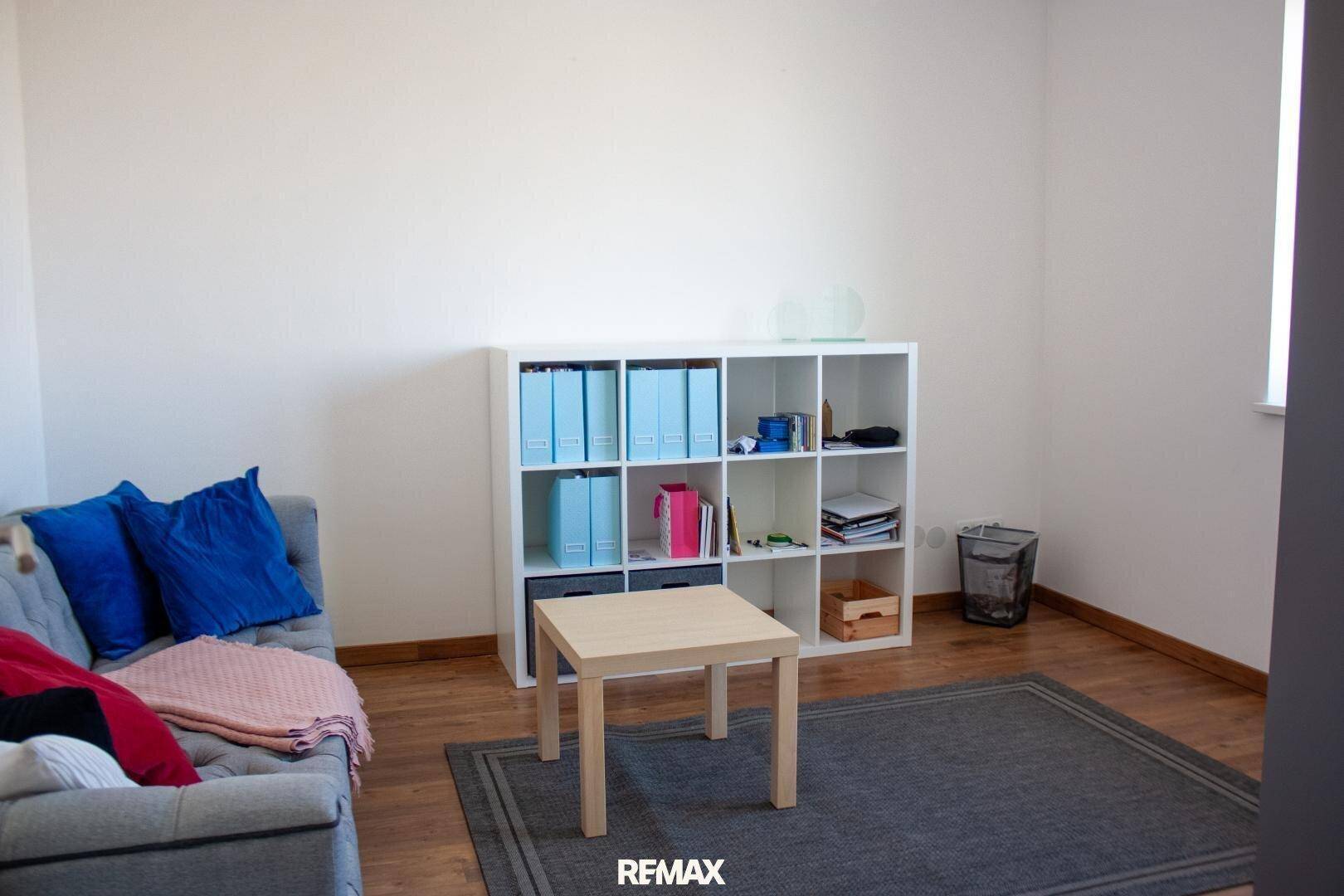 Einfaches Zimmer mit Sofa, Regal und kleinem Tisch, vielseitig nutzbar.