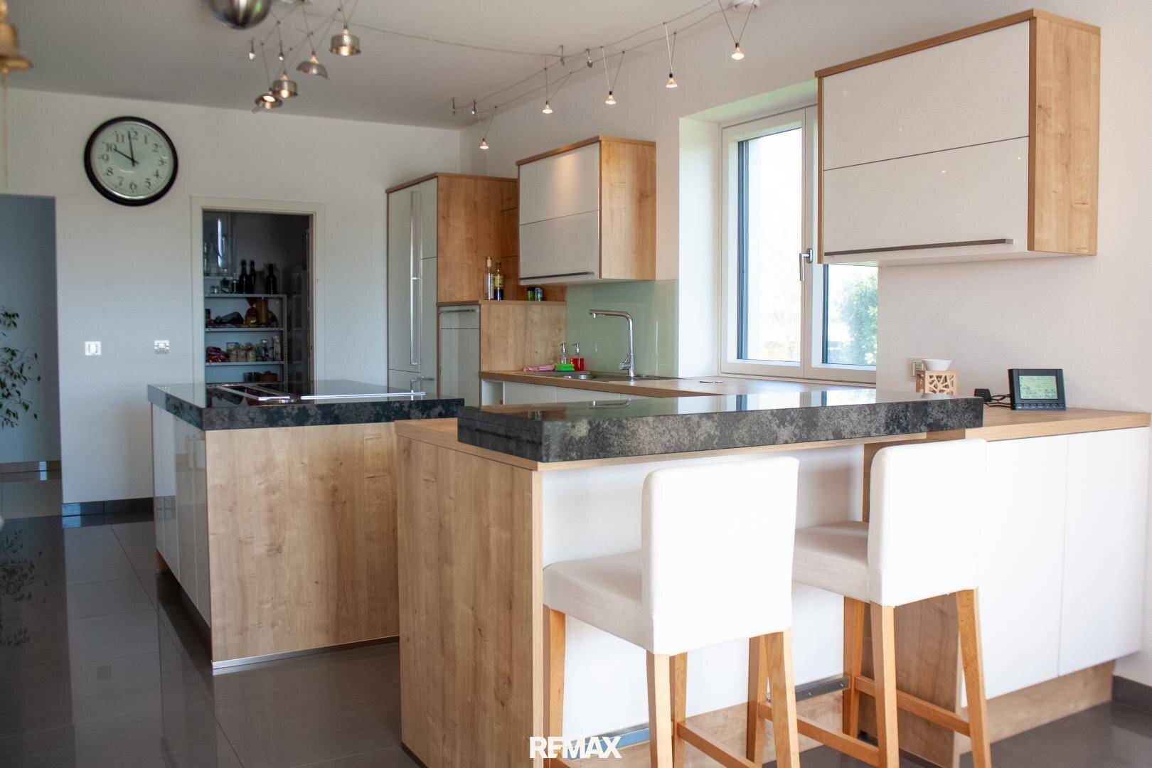Moderne Küche mit Holz- und Weißfronten, dunklen Arbeitsplatten und integrierter Frühstücksbar.