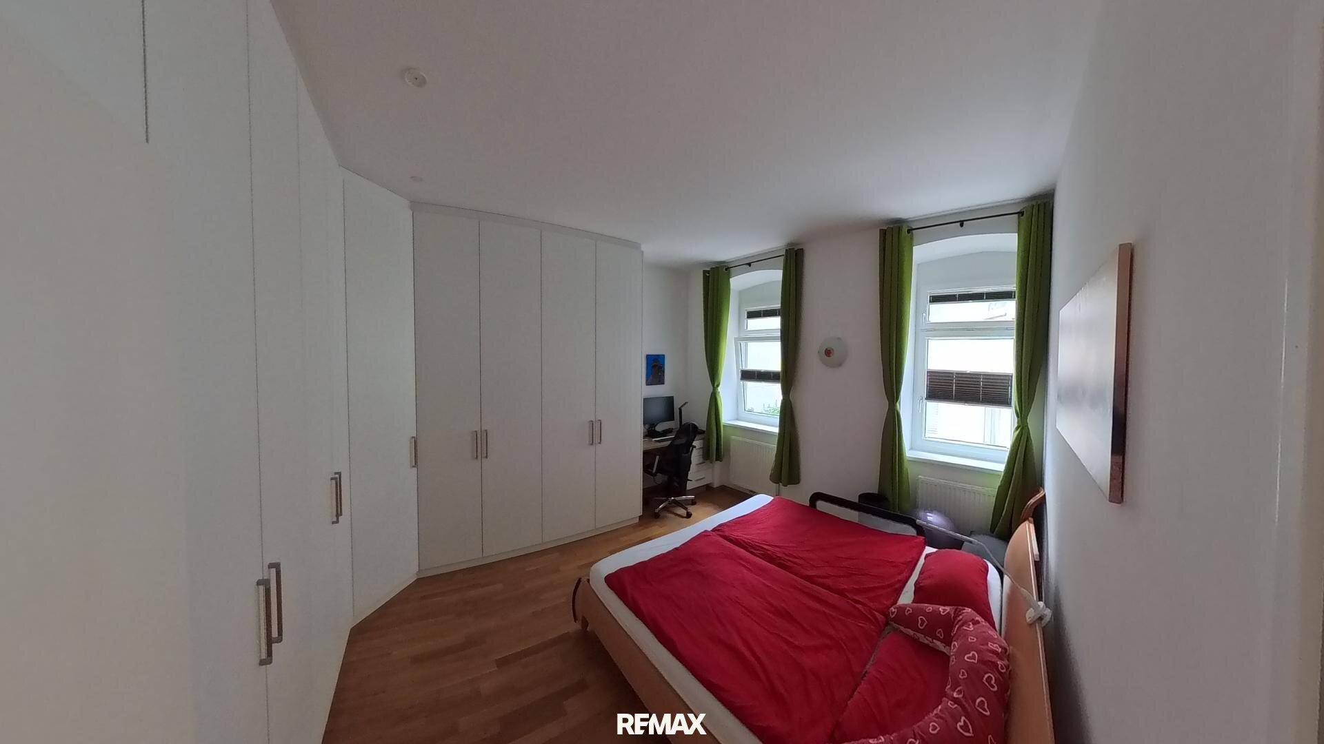 Geräumiges Schlafzimmer mit rotem Bett, Holzboden und einem großen, weißen Einbauschrank.