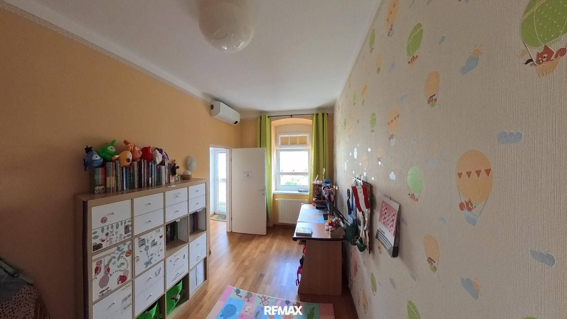 Kinderzimmer mit bunter Tapete, Holzboden, Spielzeugregal und einem Fenster, ausgestattet mit Klimaanlage.